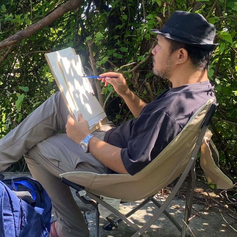 John Pabrua painting outdoors in a folding chair